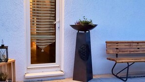 Taloon johtava sisäänkäynti, jossa on liukuovet, ruukkuistutettu kasvi, penkki ja pieni pöytä, jonka päällä on lyhty.