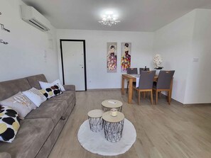 Un salon comprenant un canapé, une table à manger avec des chaises, une petite table basse et un tapis blanc.