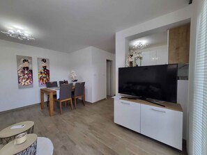 Una sala de estar moderna con comedor, televisión de pantalla plana y zona de cocina.