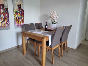 Un coin repas avec une table en bois, des chaises à revêtement gris, un vase avec des fleurs blanches et une bouteille de vin.