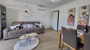 A modern living room with a sofa, a round coffee table, a dining table with chairs, a wall clock, and two paintings. - Holiday flat just 200m from the beach (Vantačići)