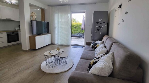 A modern living room with a sofa, a coffee table, a TV, and a kitchen area with cabinets and a refrigerator. - Holiday flat just 200m from the beach (Vantačići)