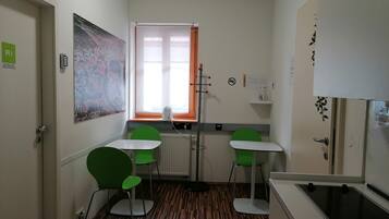 A small, modern kitchen with two green chairs, a white table, and a window with orange curtains.