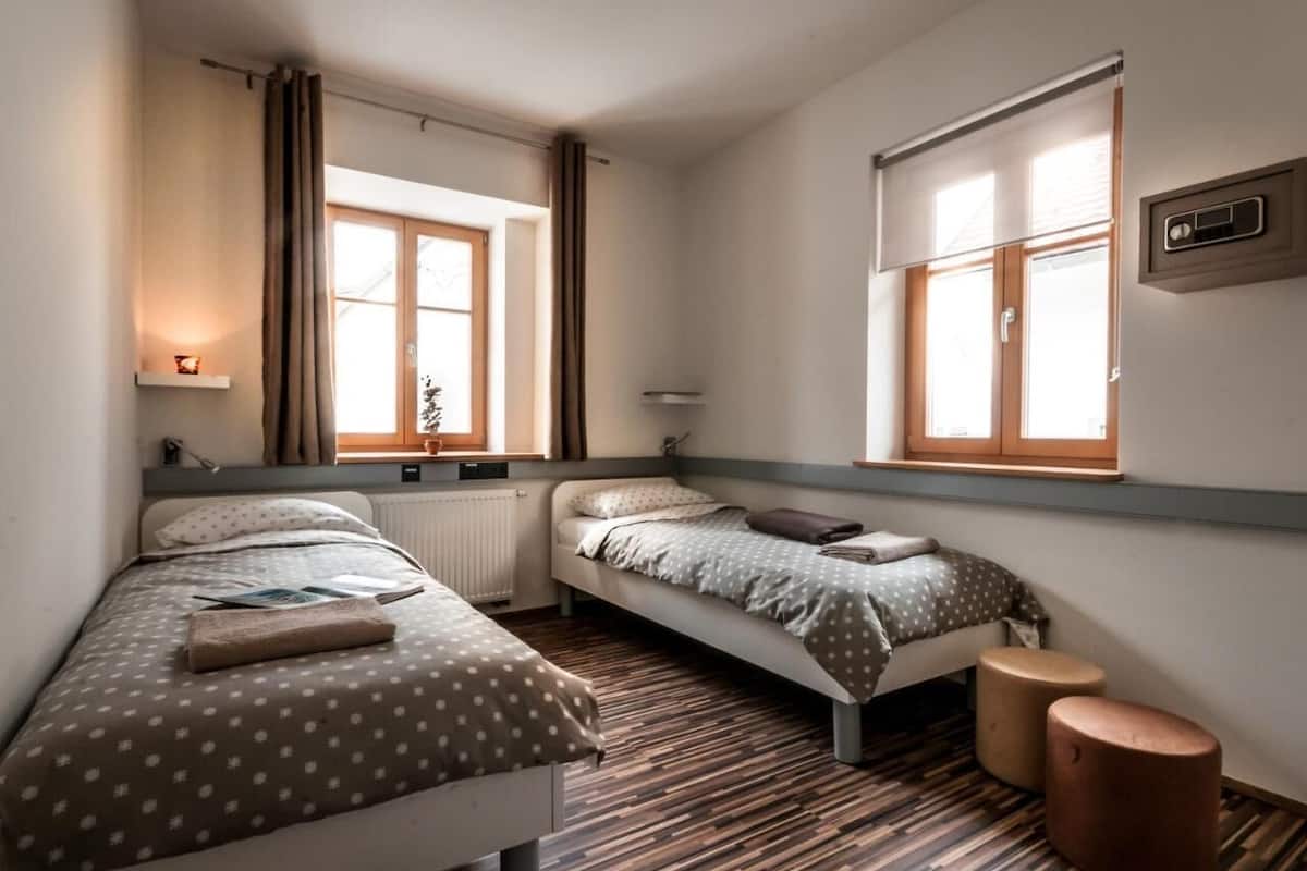 Ein Schlafzimmer mit zwei Einzelbetten, einem Fenster, einer Heizung und einem kleinen Tisch.