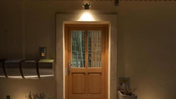 Una puerta de madera con un panel de vidrio, flanqueada por dos macetas, que da acceso a un vestíbulo empedrado.