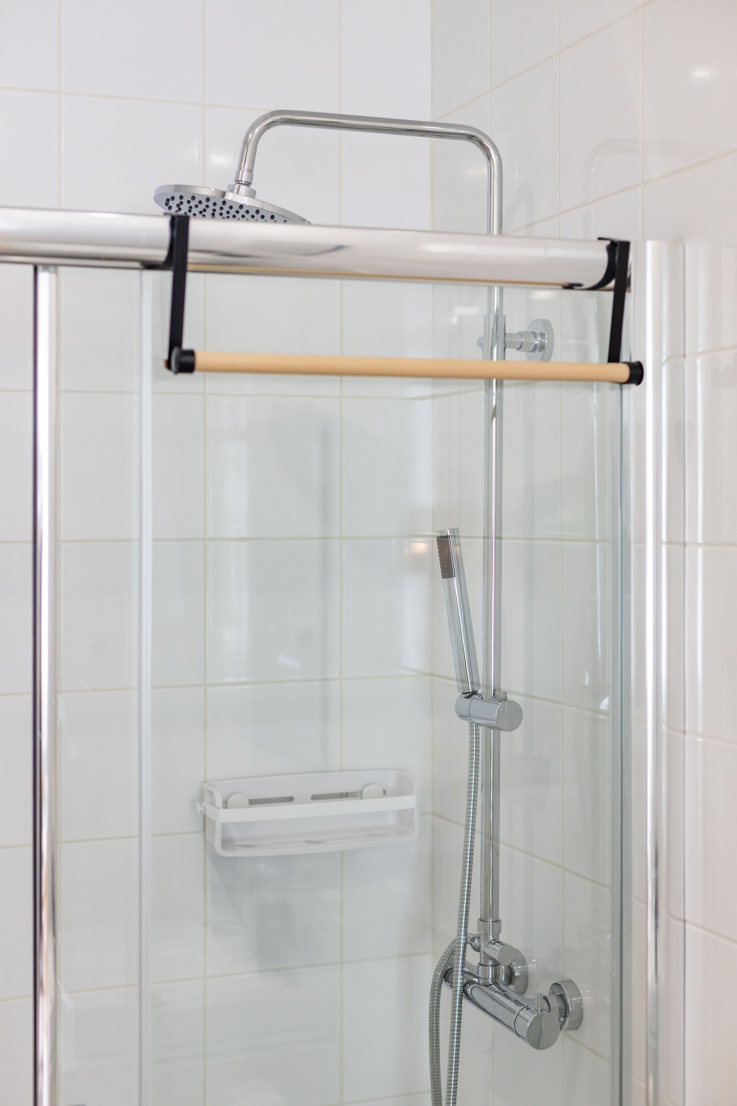 A glass-enclosed shower with a handheld showerhead, a towel rack, and a soap dish.
