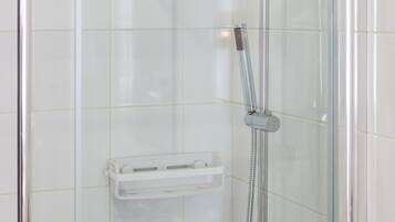 A glass-enclosed shower with a handheld showerhead, a towel rack, and a soap dish.