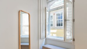 Ein Zimmer mit einem großen Spiegel, einer Bank und einem Fenster mit Blick auf ein Gebäude mit blauen Fliesen.