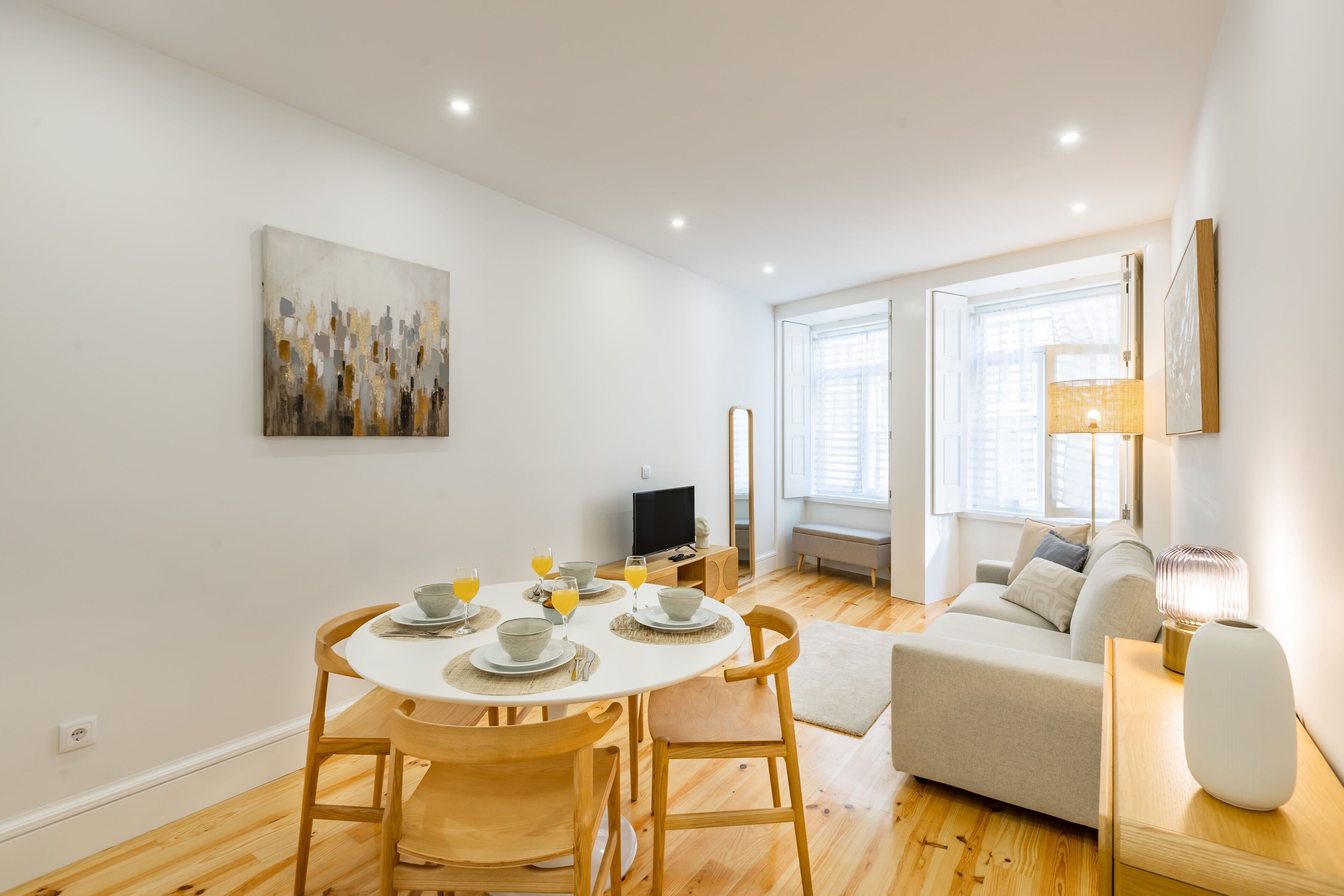 A modern living room with a dining area, wooden flooring, a sofa, a TV, and a painting on the wall.