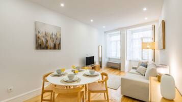 A modern living room with a dining area, wooden flooring, a sofa, a TV, and a painting on the wall.