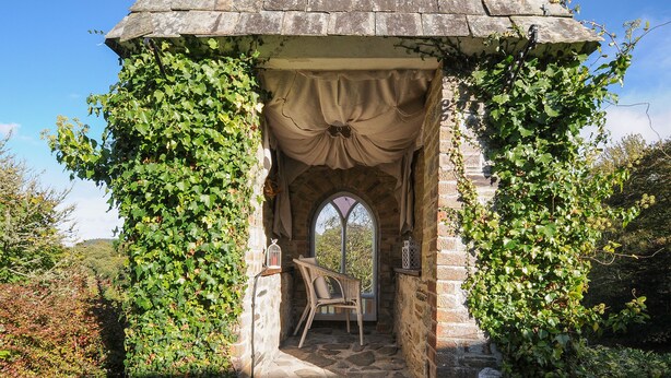A stone gazebo with a covered entrance, a wicker chair, and a birdcage. - The Wagon House (Launceston)