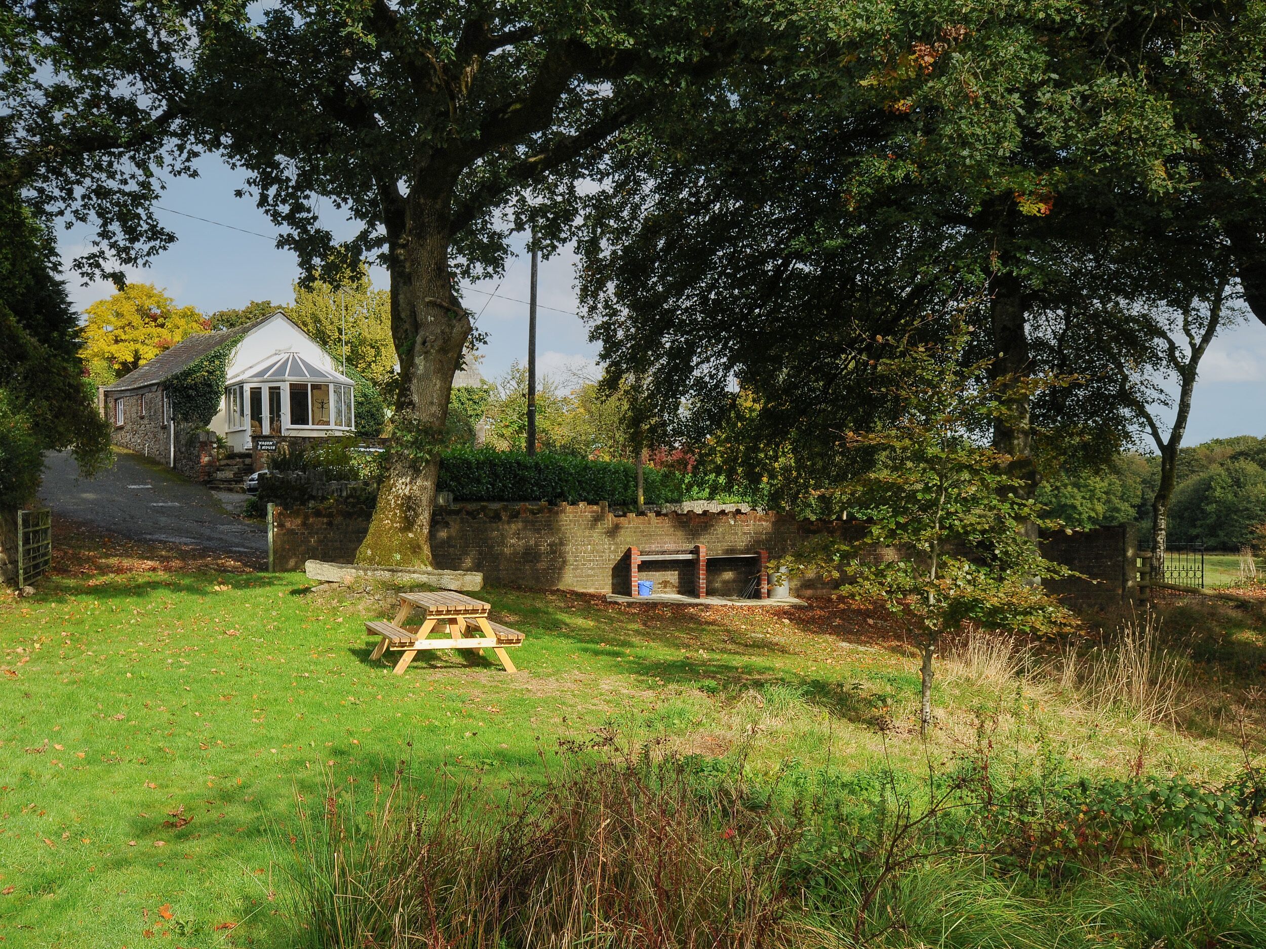 A rustic stone building with a thatched roof, a wooden bench, and a stone wall.