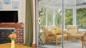 A conservatory with wicker furniture, a fireplace, and artwork on the walls. - The Wagon House (Launceston)