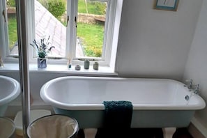 A bathroom with a freestanding bathtub, a window with a view of a garden, and a small shelf with decorative items. - 3 Bed Cottage-sleeps 6-country Views-pet Friendly (Sunderland)