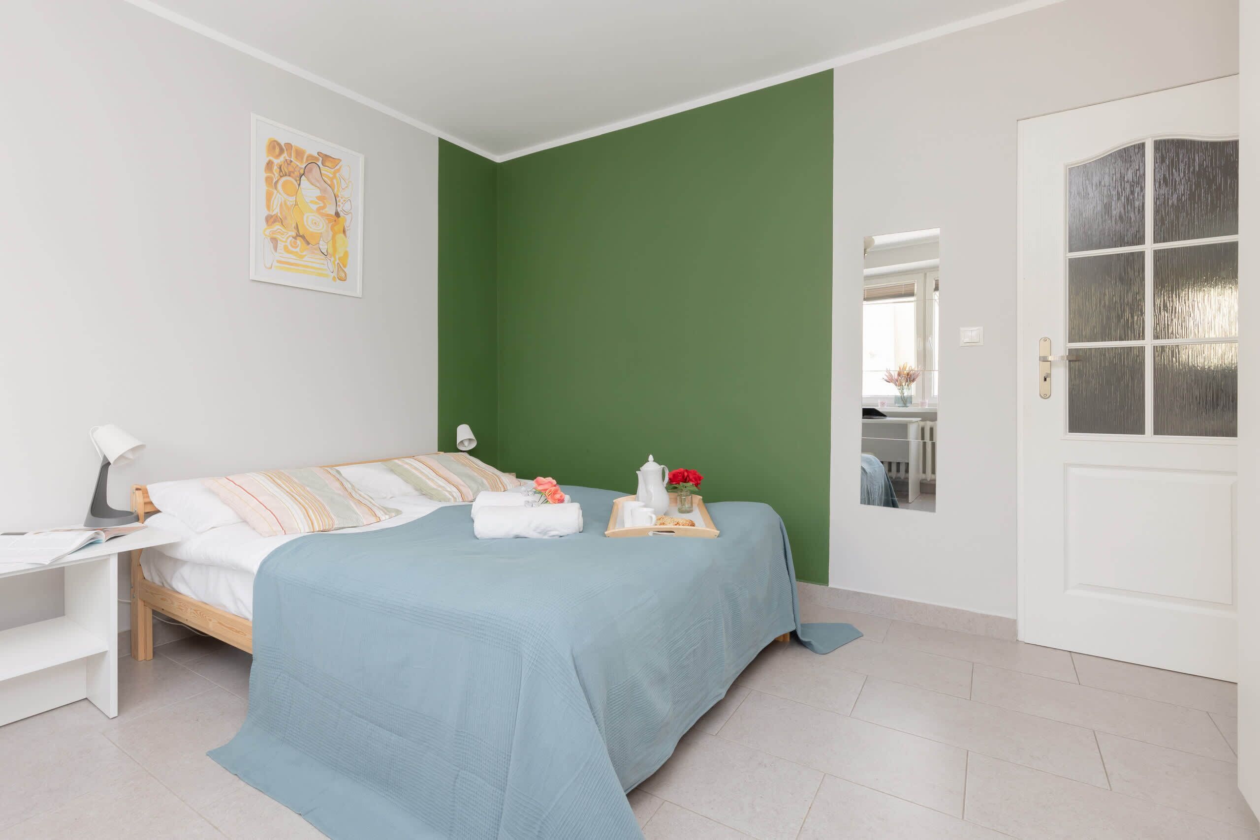 A neatly arranged bedroom with a bed, bedside table, and a green accent wall.