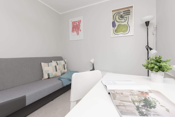 A modern, minimalist living room with a grey sofa, a white table, and two abstract wall art pieces.