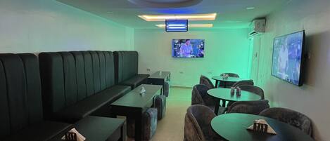 Un'area lounge moderna con posti a sedere e tavoli, una TV a schermo piatto montata a parete e illuminazione d'ambiente.