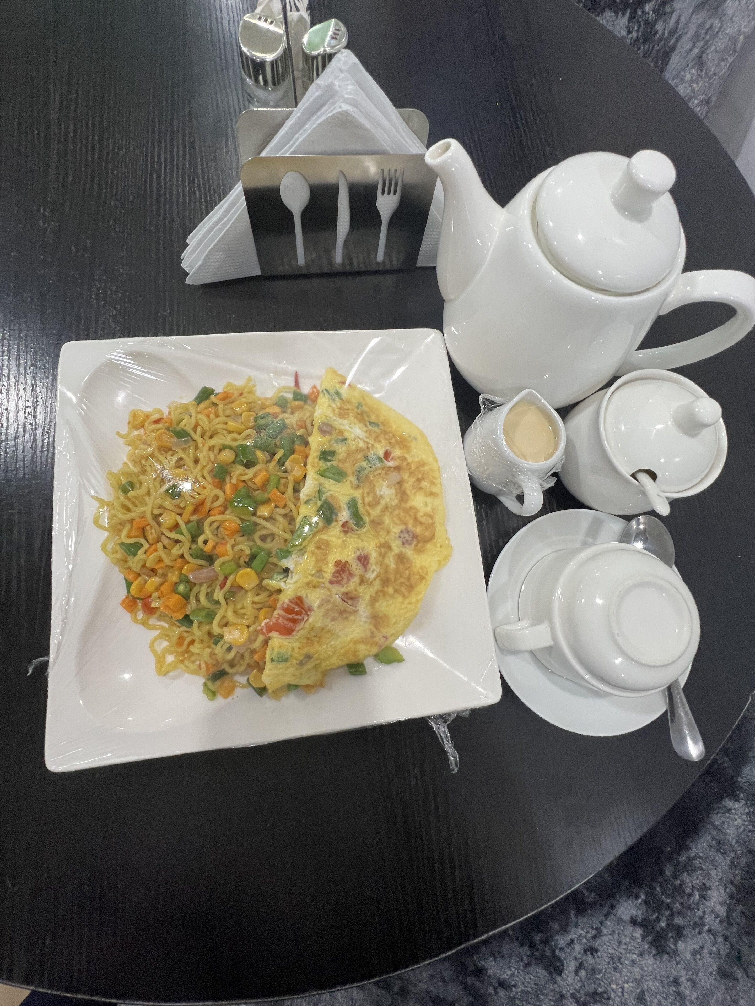 Une table avec une assiette de nourriture, une théière, des tasses et une couverts.