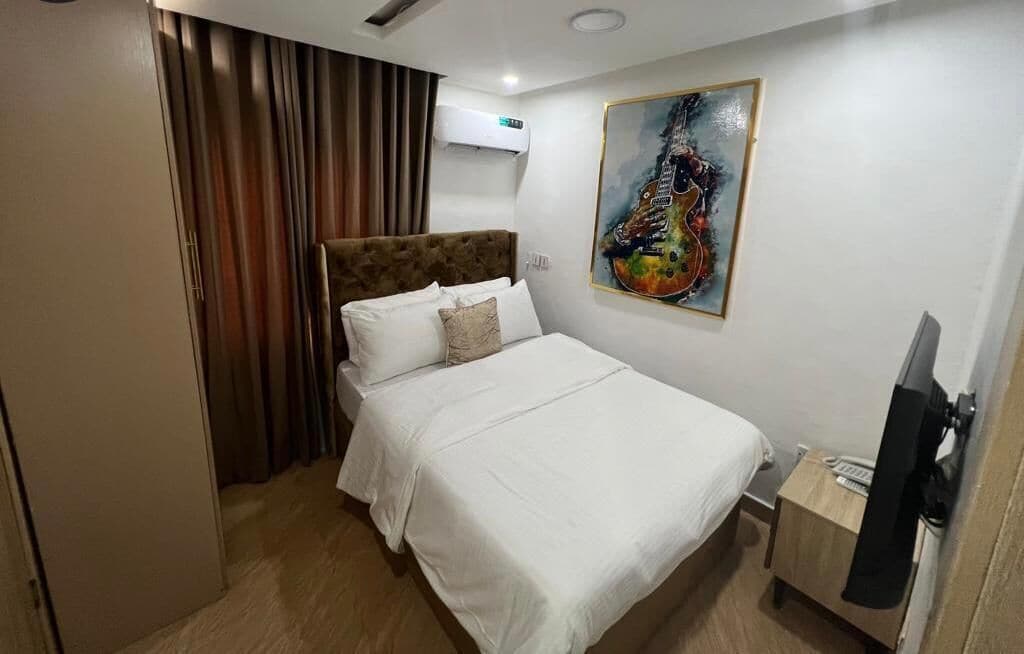 Una habitación de hotel con cama, un cuadro, aire acondicionado y televisión.