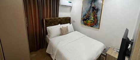 A hotel room with a bed, a painting, an air conditioner, and a TV.