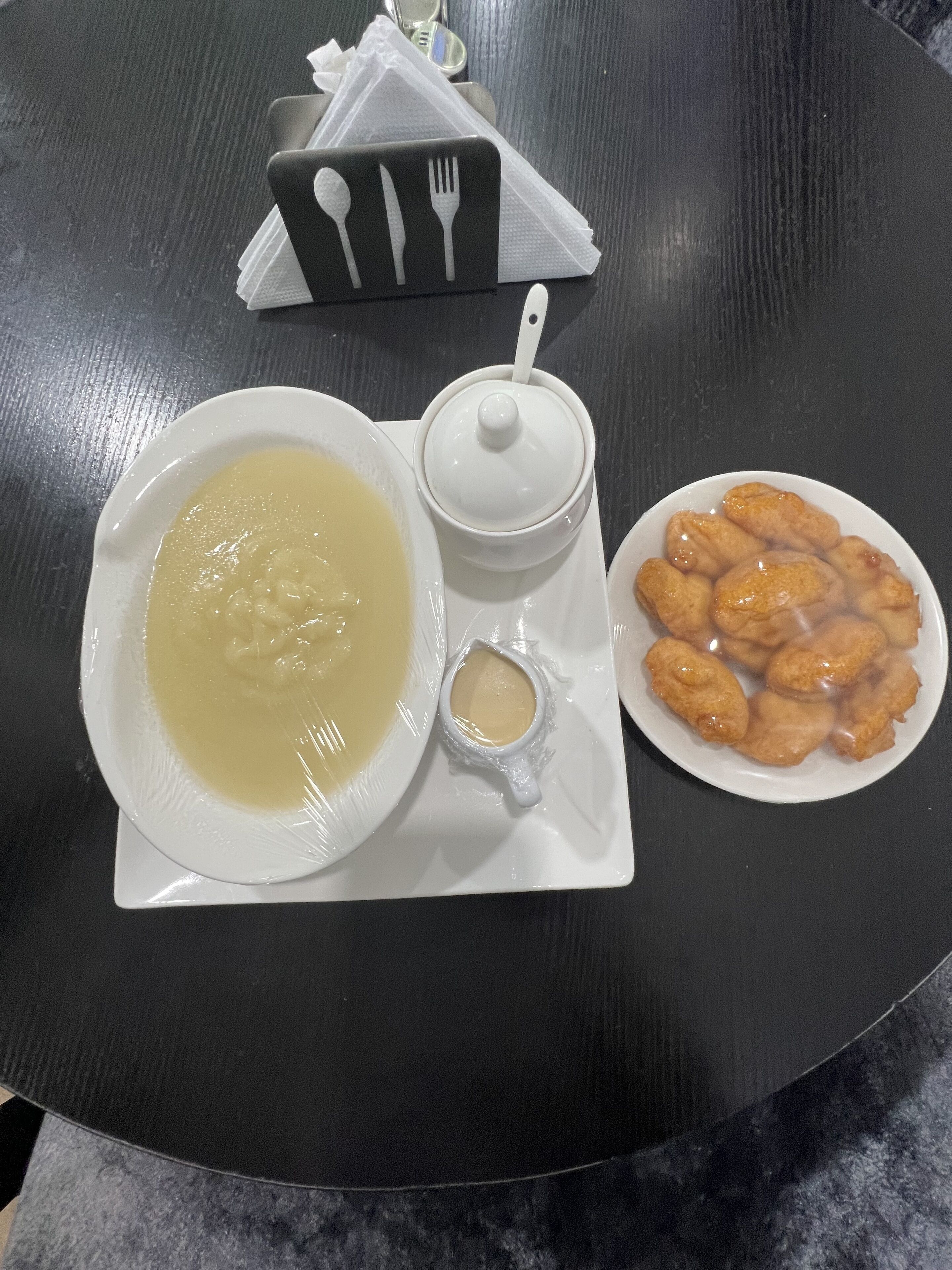 Una mesa con un plato de sopa, un cuenco pequeño de salsa y un plato de comida frita.