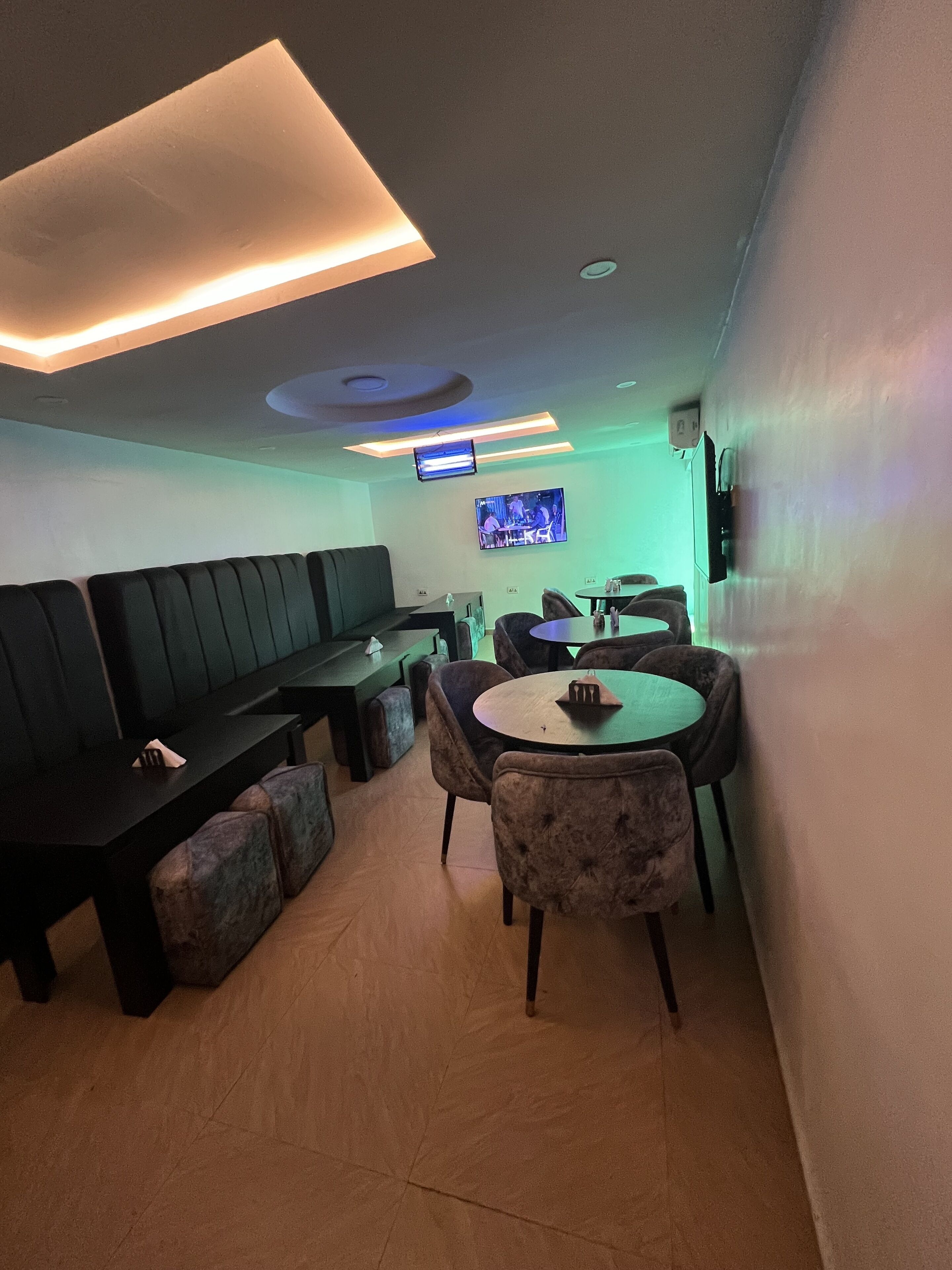 A modern lounge area with a long bench, round tables, and cushioned seating.