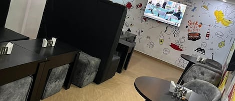 A modern restaurant with a TV screen, grey upholstered chairs, and a wall decorated with food-related illustrations.