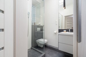 A modern bathroom with a glass-enclosed shower, a white toilet, and a sink with a mirror. - Stylish Studio in Krakow | Close to Main Station and Market Square (Kraków)