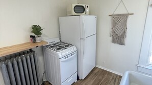 A compact kitchen with a gas stove, a white refrigerator, a microwave, a small plant, and a macrame wall hanging. - Downtown Colorado Springs Studio (Colorado Springs)