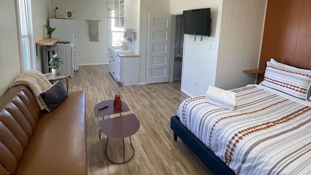 A compact hotel room with a bed, a sofa, a small table, and a kitchenette. - Downtown Colorado Springs Studio (Colorado Springs)