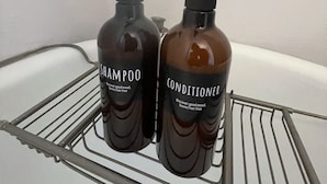 Two bottles of shampoo and conditioner on a metal shelf in a bathroom. - Downtown Colorado Springs Studio (Colorado Springs)