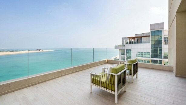 Un balcon avec vue sur l’océan et un bâtiment moderne aux fenêtres en verre.