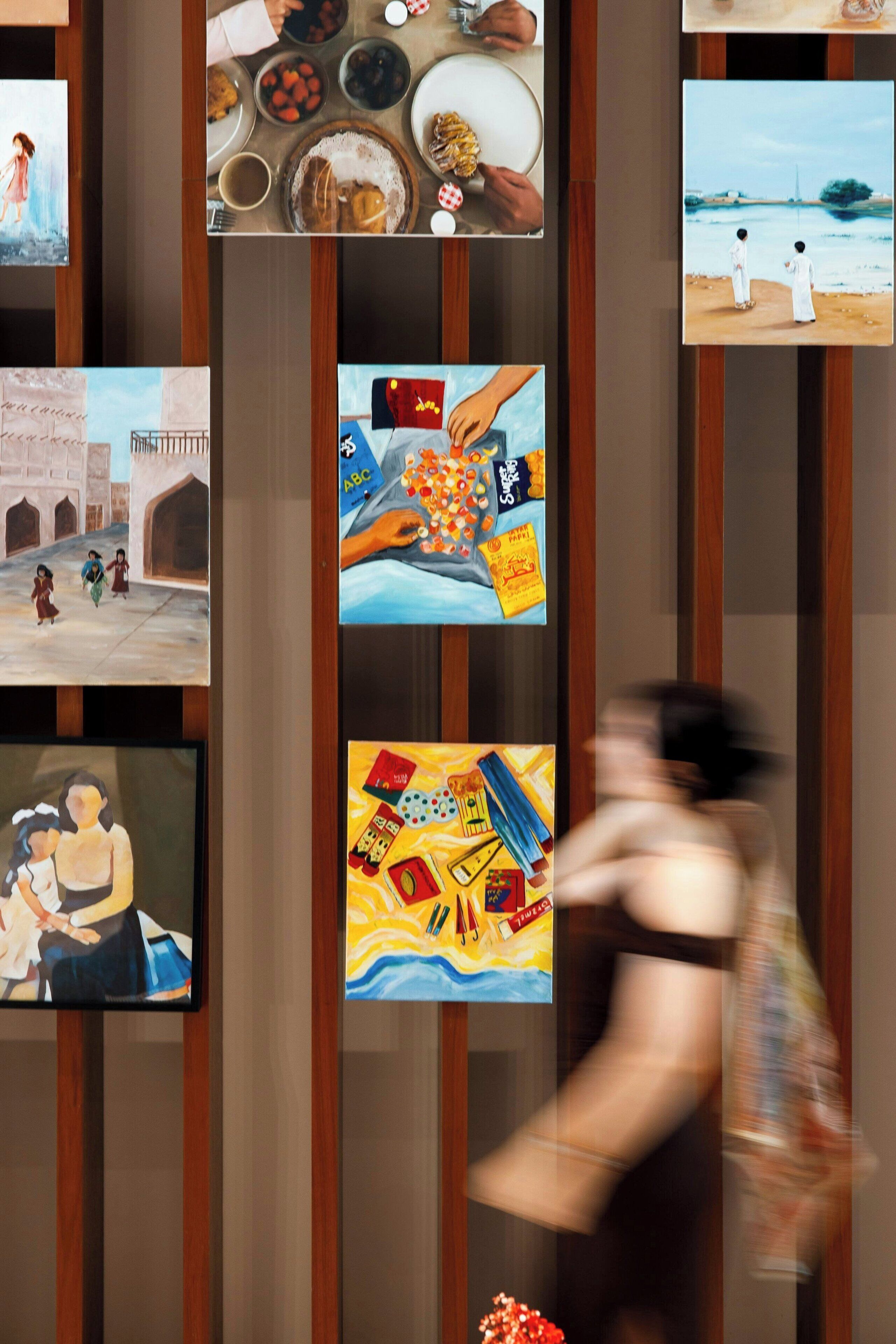 Una pared con varios cuadros enmarcados, incluyendo una pintura de una mujer y un niño, una escena con comida, y una representación de una mano sosteniendo una bandera.