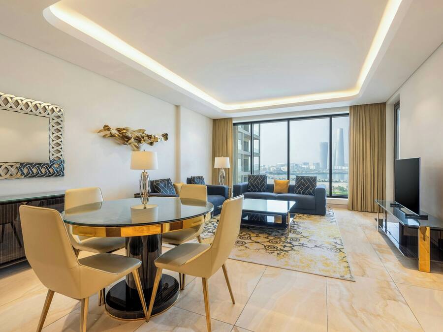 Ein modernes Hotelzimmer mit Essbereich, einer Couch, einem Fernseher und einem großen Fenster mit Blick auf die Stadt.