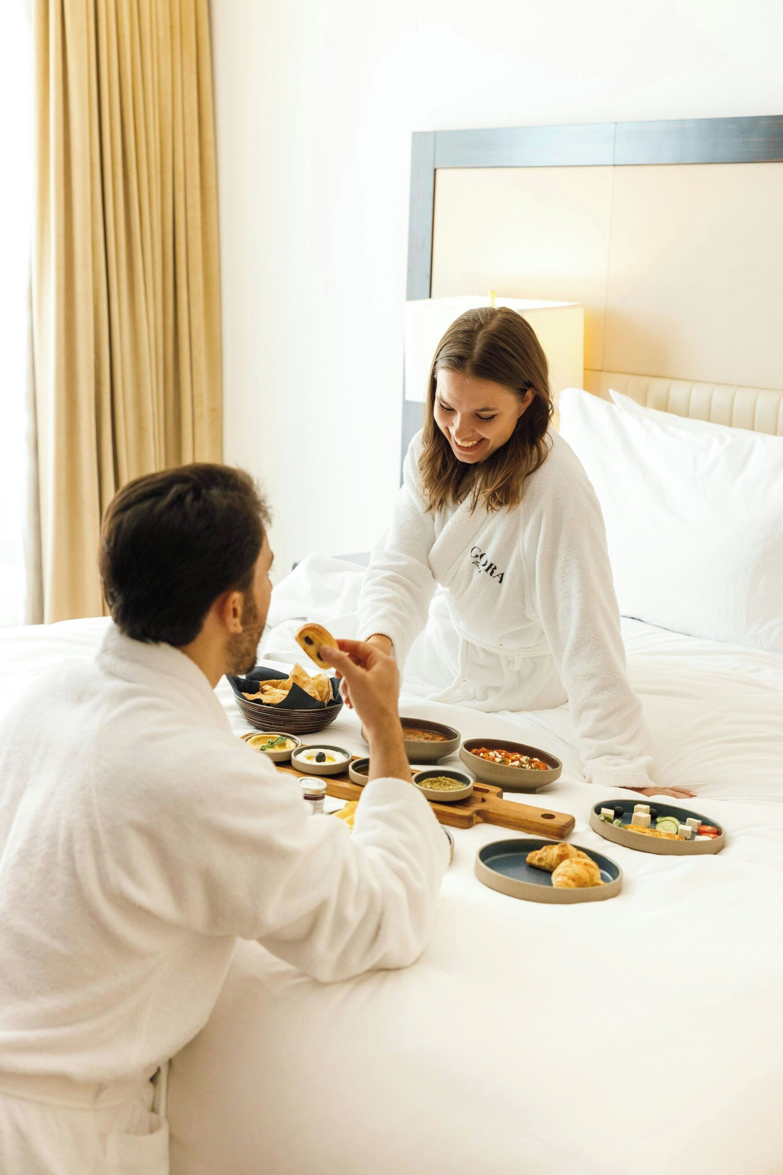 Une chambre d’hôtel avec un lit, une table de chevet sur laquelle se trouvent des articles pour le petit-déjeuner et une lampe.