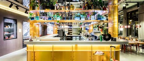 Un espacio interior de varios niveles con un mostrador amarillo central, diferentes zonas de estar y numerosas plantas en macetas.