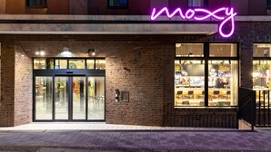 A building with a neon sign reading "moxy" and a glass door entrance. - Moxy Dortmund (Dortmund)