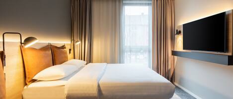 A hotel room with a bed, a TV mounted on the wall, a desk, and a chair.