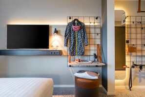 A modern hotel room with a large flat-screen TV, a desk with a laptop, and a hanging coat rack. - Moxy Dortmund (Dortmund)