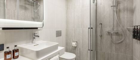 A modern bathroom with a white sink, toilet, and glass shower enclosure.
