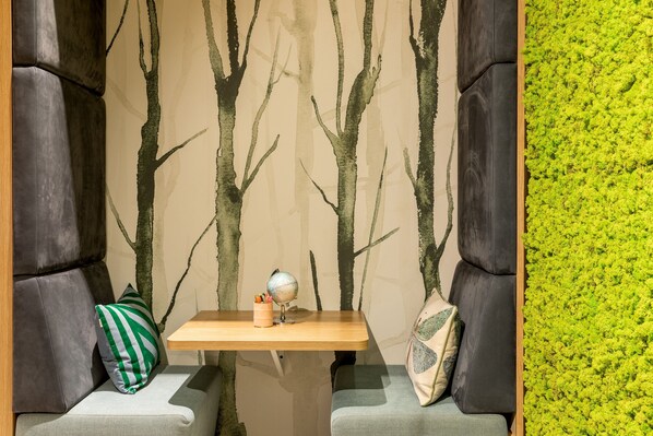 A seating area with a wooden table, two cushioned chairs, and a wall with a tree mural.