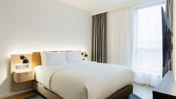 A hotel room with a large bed, a nightstand with a lamp, a TV, and a window with curtains.