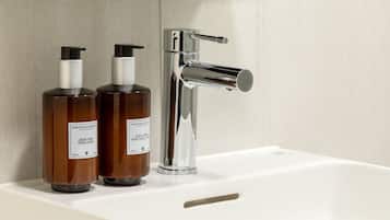 Une salle de bain avec un lavabo blanc, deux flacons de savon marron et un robinet chromé.