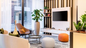 A modern living room with a large window, a flat-screen TV, a potted plant, a sofa, and a coffee table. - Residence Inn by Marriott Dortmund (Dortmund)