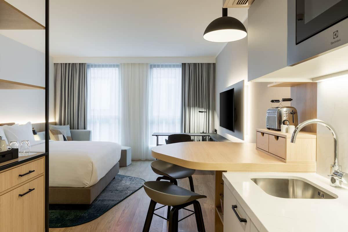 A hotel room with a bed, a desk, a sink, and a television.