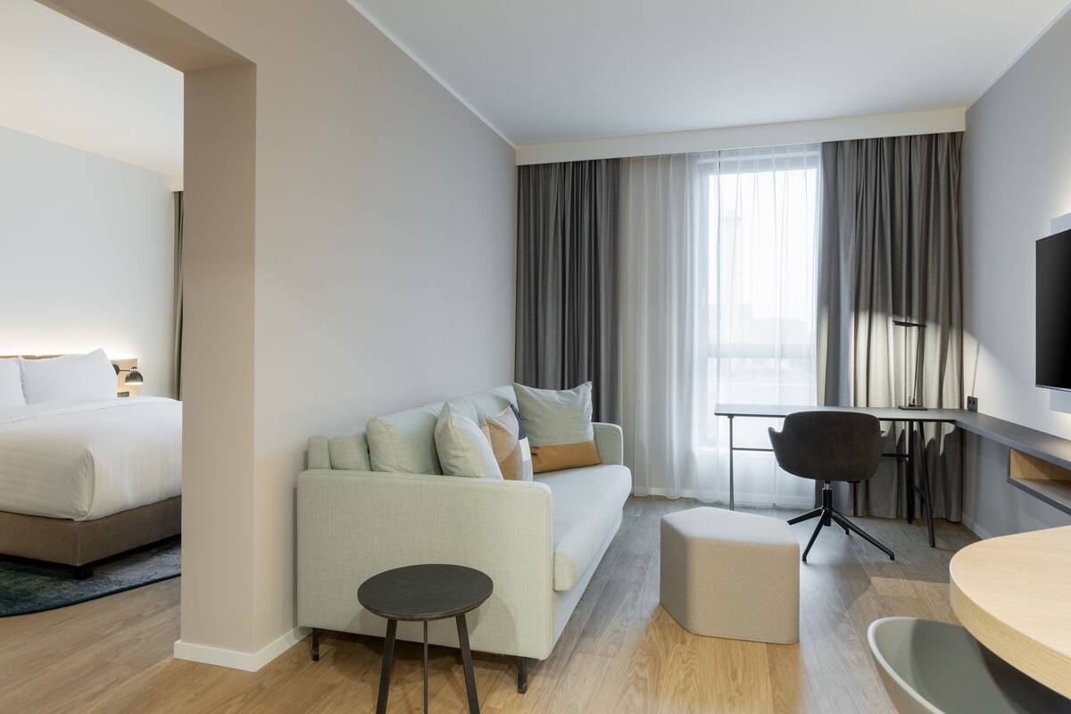 A modern hotel room with a bed, a sofa, a desk, and a TV.