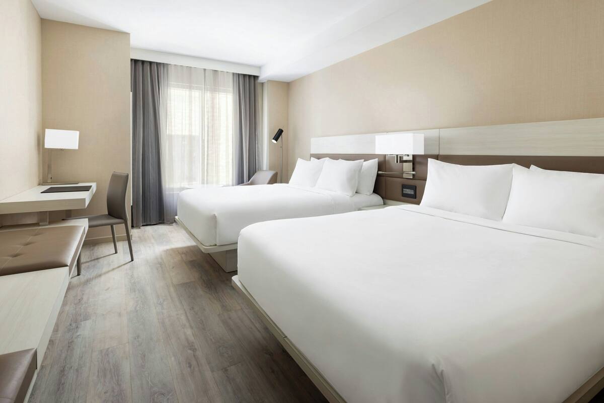 A hotel room with two beds, a desk, and a chair.