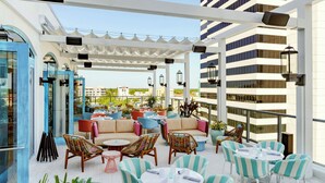 Una terraza en la azotea con mobiliario exterior, incluyendo sillas y mesas a rayas, y vistas a la ciudad.