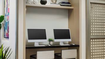 Un espacio de oficina moderno con dos computadoras de escritorio, una planta pequeña y una estantería con objetos decorativos.