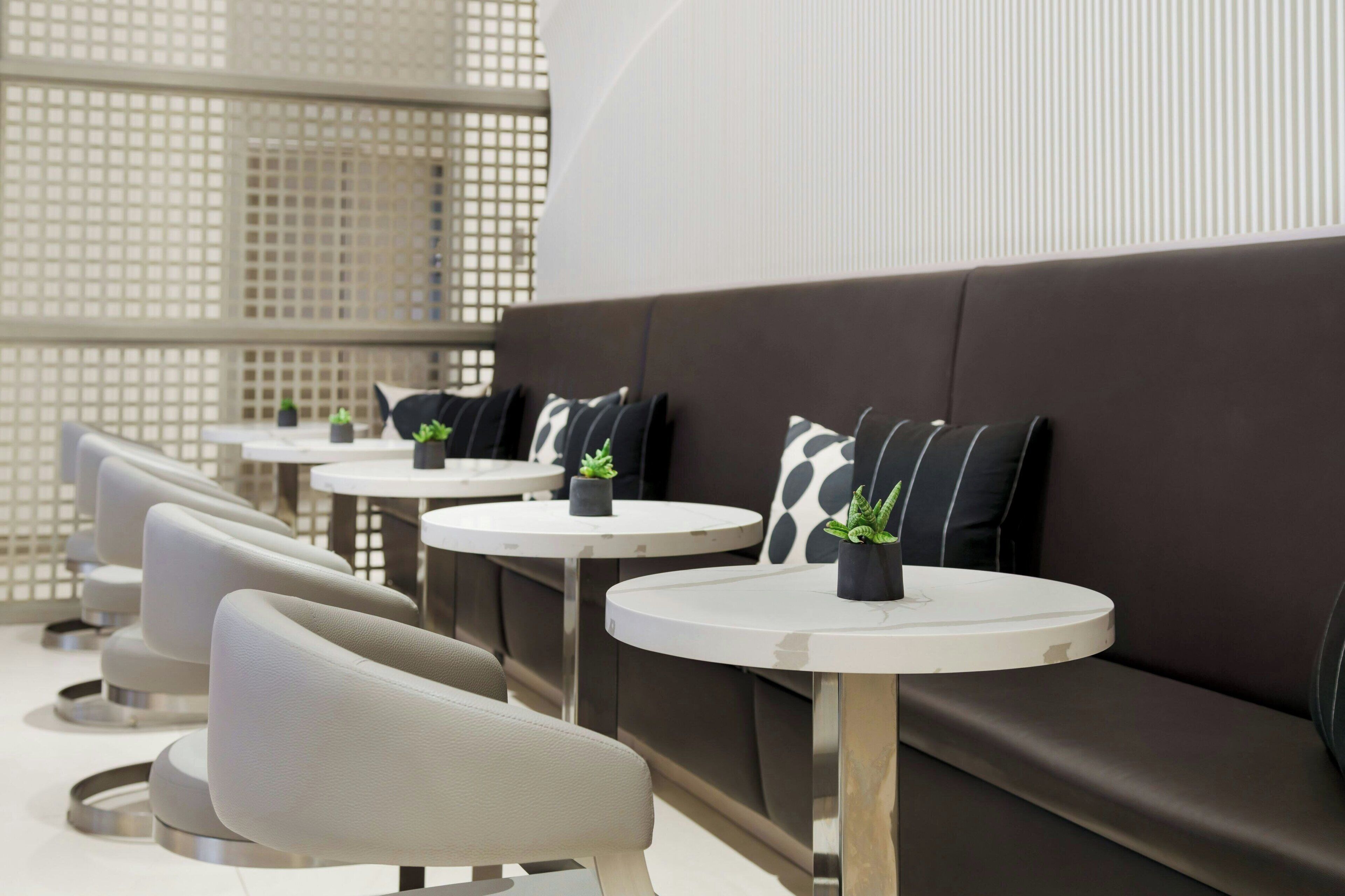 Een moderne zithoek met banken en ronde tafels, elk voorzien van een kleine plant.